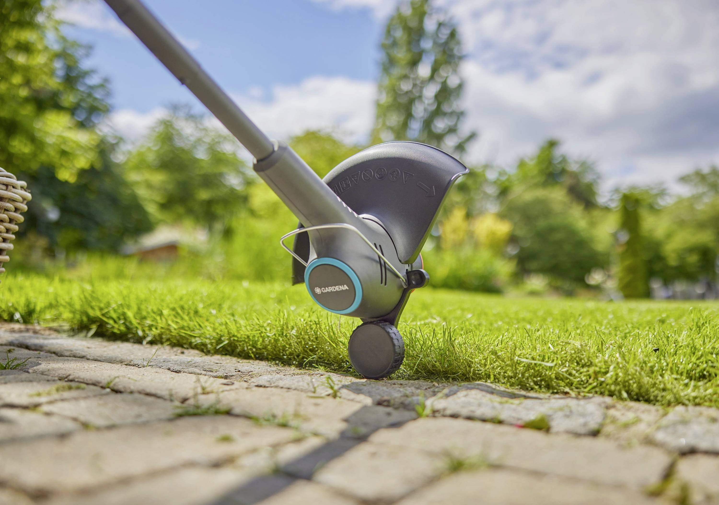 Rasenmäher schneidet präzise den Rand eines Rasens entlang eines gepflasterten Weges in einem sonnigen Garten.