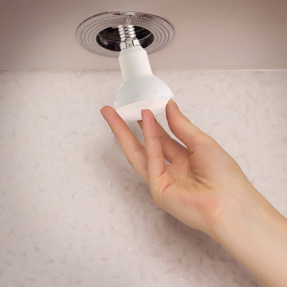 Eine Hand dreht eine Glühbirne in eine Deckenfassung ein.