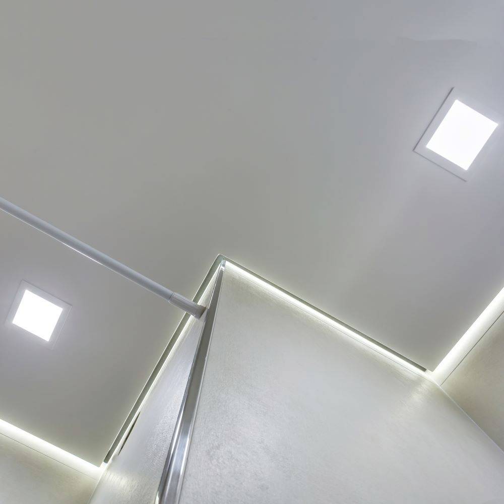 Weiße Decke mit integrierten quadratischen LED-Leuchten und silbernem Handlauf; modernes, schlichtes Design.