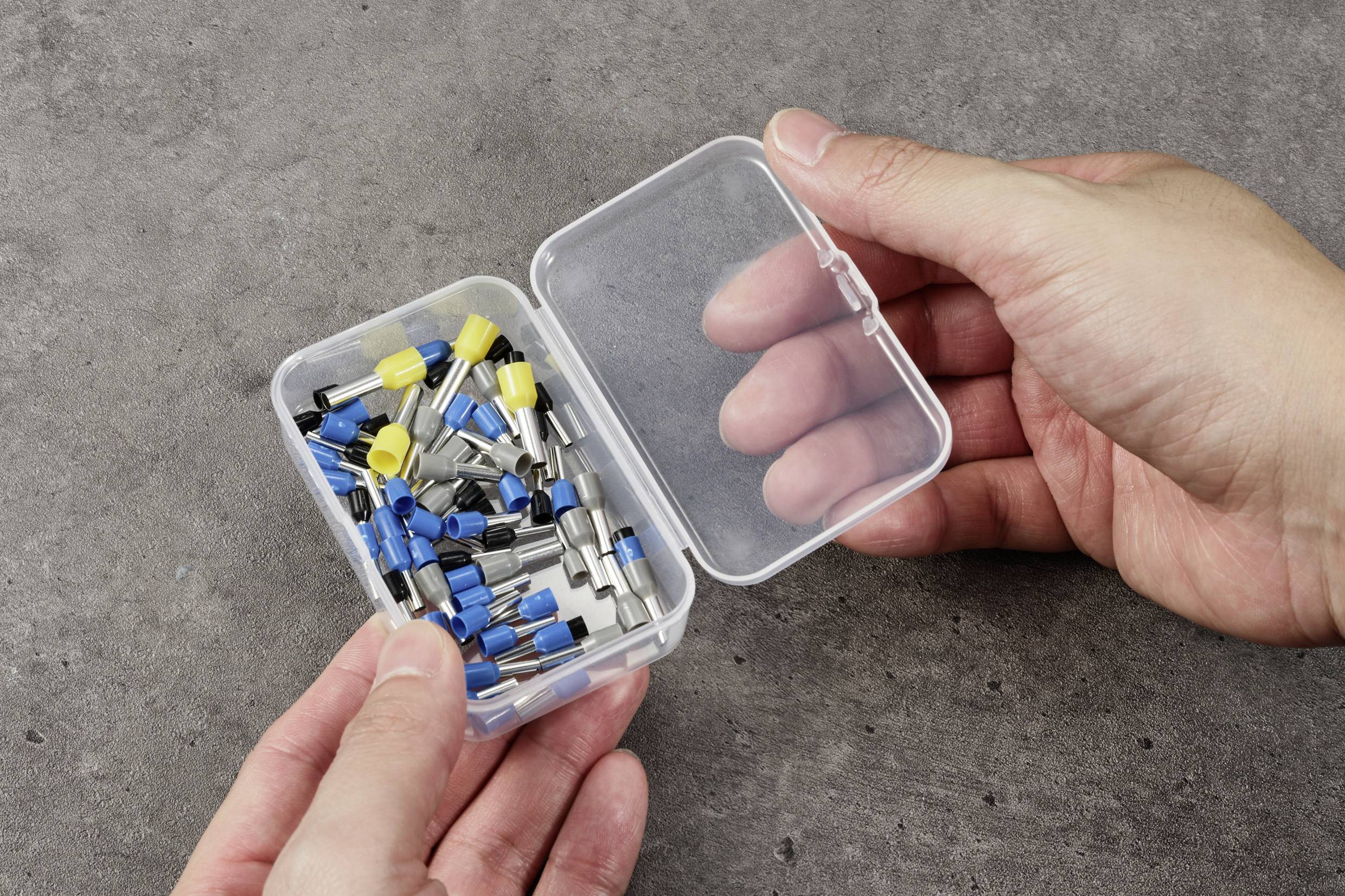 Eine Hand hält eine geöffnete Plastikbox mit verschiedenen farbigen Kabelschuhen, geeignet für elektrische Verbindungen.