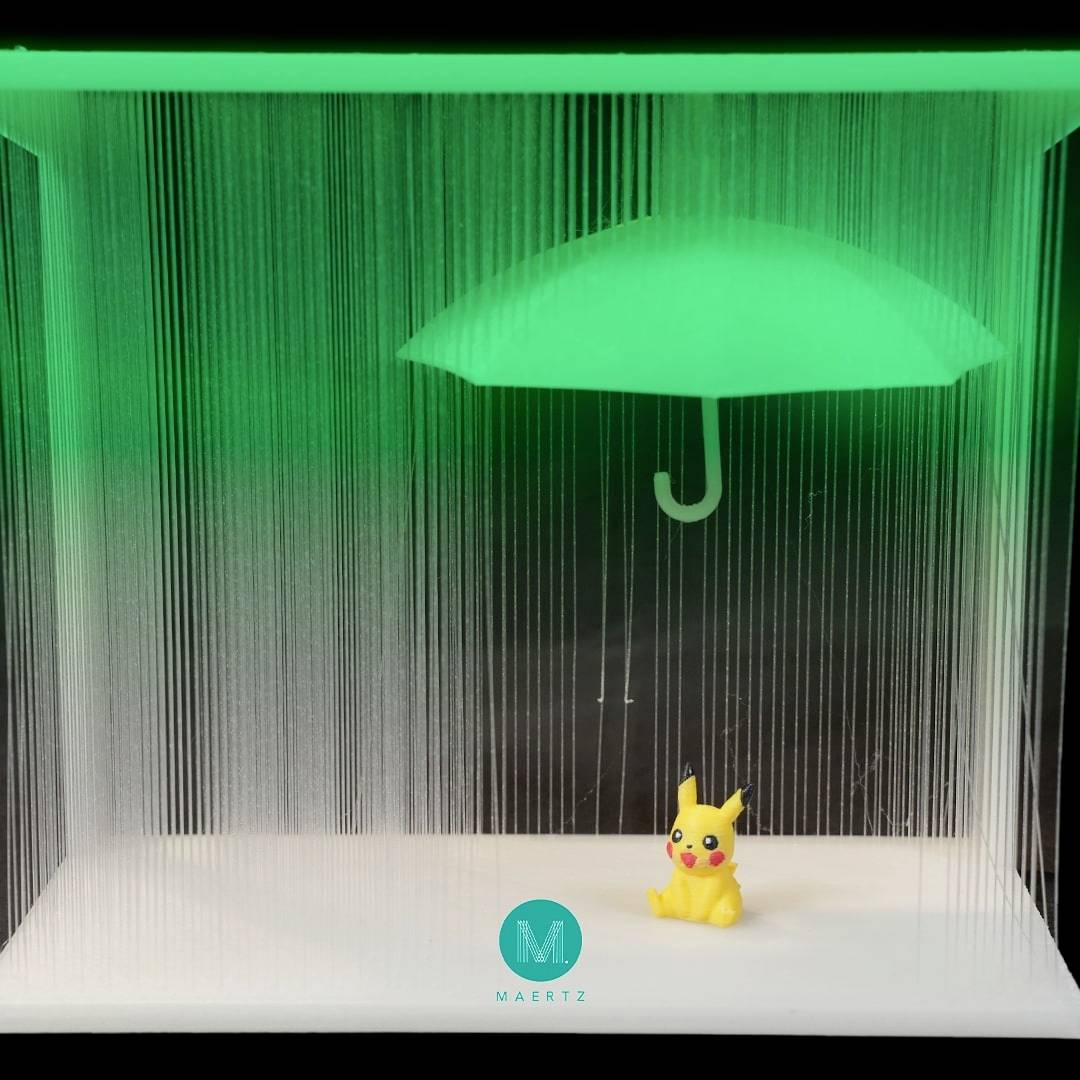 Eine kleine gelbe Figur sitzt unter einem beleuchteten grünen Regenschirm, der in einem dunklen Raum hängt.