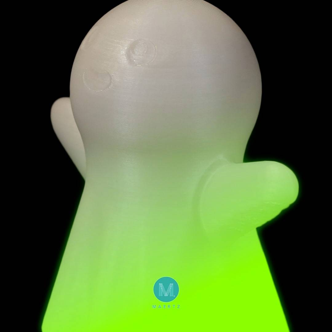 Eine weiße, spukhafte Figur mit grün leuchtendem Sockel, auf schwarzem Hintergrund. Unten ist ein blaues Logo mit einem 'M' sichtbar.