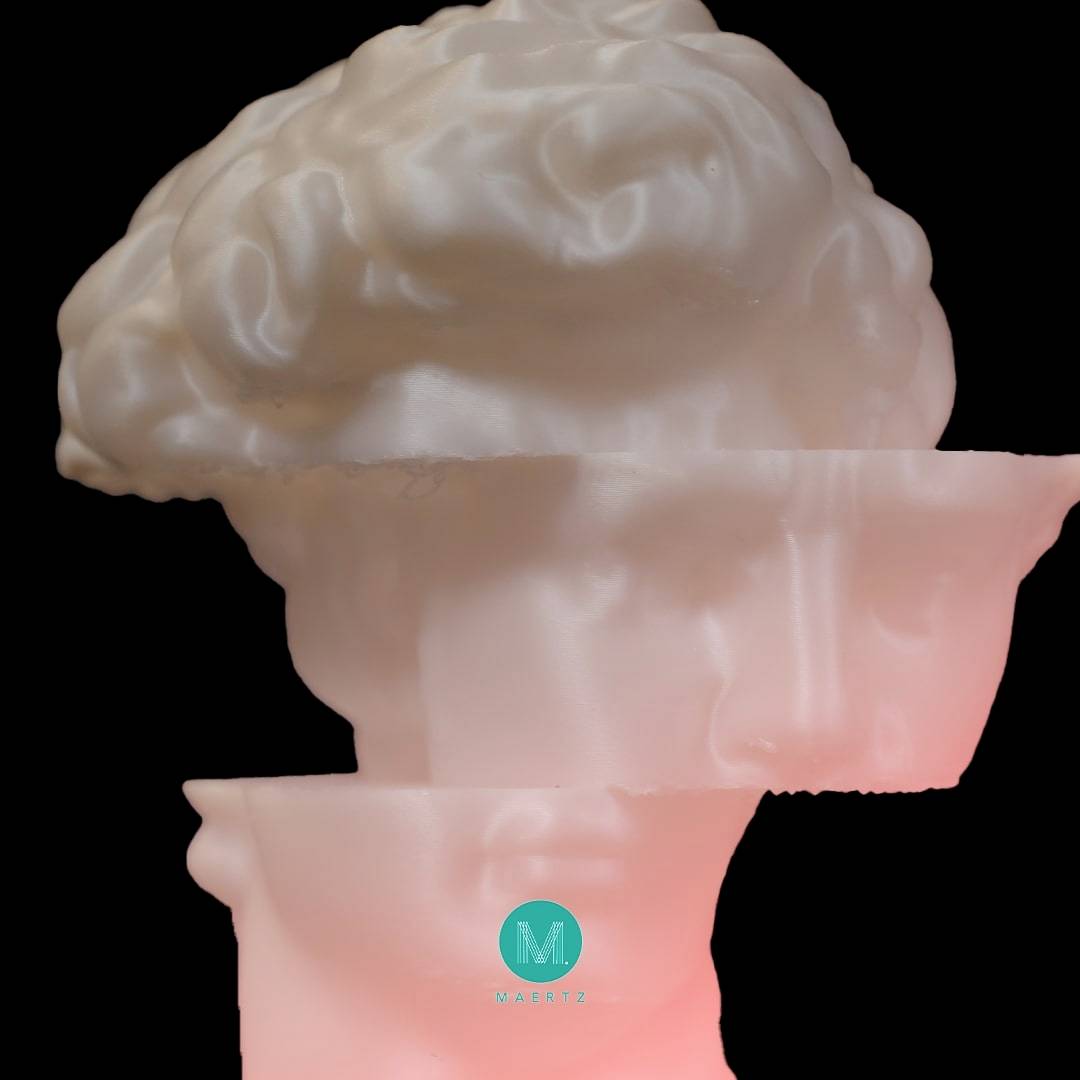 Eine Skulptur eines Kopfes mit abgetrenntem Oberteil, das ein Gehirn freilegt, beleuchtet in Rosa. Ein Logo 'M' unten sichtbar.