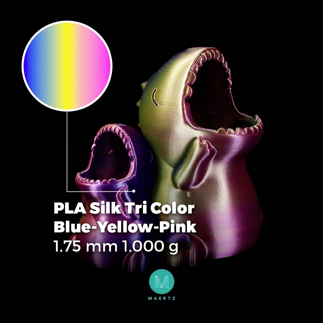 Zwei bunte Figuren in schillerndem Blau, Gelb und Pink. Text daneben: 'PLA Silk Tri Color Blue-Yellow-Pink 1.75 mm 1.000 g'. 