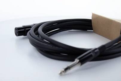Ein schwarzes Audiokabel mit einem 3-poligen XLR-Stecker auf einer Seite und einem Klinkenstecker auf der anderen Seite liegt auf einem Tisch.
