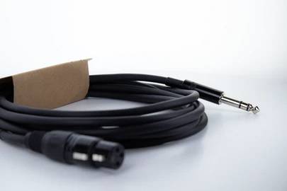 Ein schwarzes Audiokabel mit einem XLR- und einem Klinkenstecker liegt locker gerollt auf einer weißen Oberfläche.