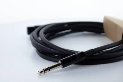 Ein zusammengerolltes schwarzes Audiokabel mit einem 6,3-mm-Stecker an einem Ende, auf einem weißen Hintergrund liegend.