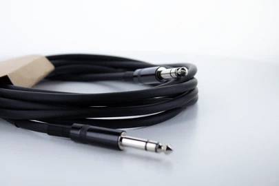 Ein schwarzes Audiokabel mit zwei silbernen Klinkensteckern, aufgerollt auf einem weißen Hintergrund.
