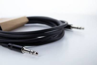 Ein langes, schwarzes Audiokabel mit zwei Klinkensteckern. Es liegt locker aufgerollt auf einem weißen Untergrund.