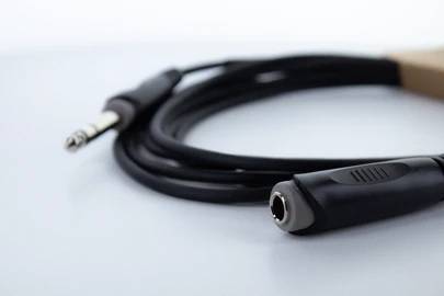 Ein schwarzes Audiokabel mit einem 6,35 mm Klinkenstecker und einer Buchse liegt gewunden auf einer ebenen weißen Oberfläche.