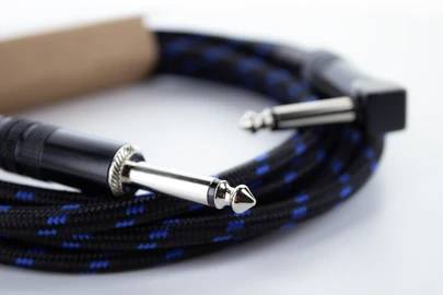 Ein blau-schwarzes Gitarrenkabel mit zwei Klinkensteckern liegt aufgerollt auf einer weißen Oberfläche.