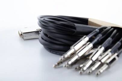 Mehrere schwarze Audiokabel mit silbernen Steckern liegen ordentlich aufgewickelt auf einer weißen Oberfläche.