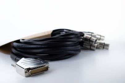 Ein Bündel schwarzer Audiokabel mit mehreren Steckern an einem Ende und einem einzelnen Metallstecker am anderen Ende liegt auf einem hellen Hintergrund.
