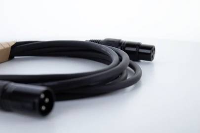 Ein schwarzes Audiokabel mit zwei Steckern, einem mit drei und einem mit vier Pins, liegt lose gewickelt auf einer weißen Oberfläche.