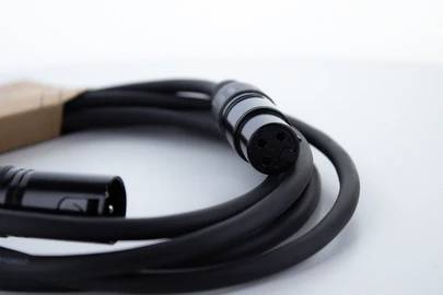 Schwarzes XLR-Kabel mit drei Pins, ausgelegt auf einem weißen Hintergrund. Verbindet Mikrofone oder Audioausrüstung für professionelle Tonübertragung.