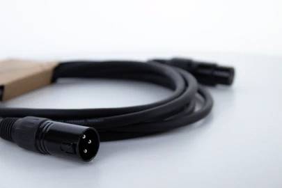 Ein schwarzes Audiokabel mit drei Pins liegt auf einer weißen Oberfläche. Links ist ein brauner Adapter an das Kabel angeschlossen.