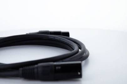 Ein schwarzes, zusammengerolltes Audiokabel mit XLR-Steckern an beiden Enden liegt auf einem weißen Hintergrund.