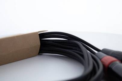 Ein Bündel schwarzer Kabel mit roten und schwarzen Steckern ragt aus einer braunen Verpackung auf einem weißen Hintergrund heraus.