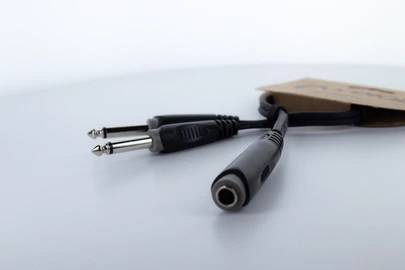 Ein Audioadapter mit zwei 6,35 mm Klinkensteckern und einer Buchse liegt auf einer weißen Oberfläche.