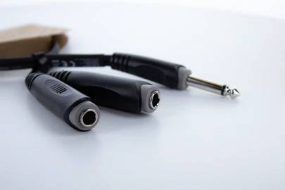 Drei Audiokabelstecker auf einer weißen Oberfläche; links zwei 3,5-mm-Buchsen, rechts ein 6,35-mm-Stecker, im Hintergrund ein Pappkarton.