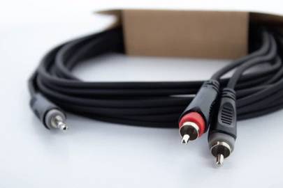 Schwarze RCA-Kabel mit roten und weißen Steckern vor einem verschwommenen Hintergrund, die aus einem Karton herausragen.