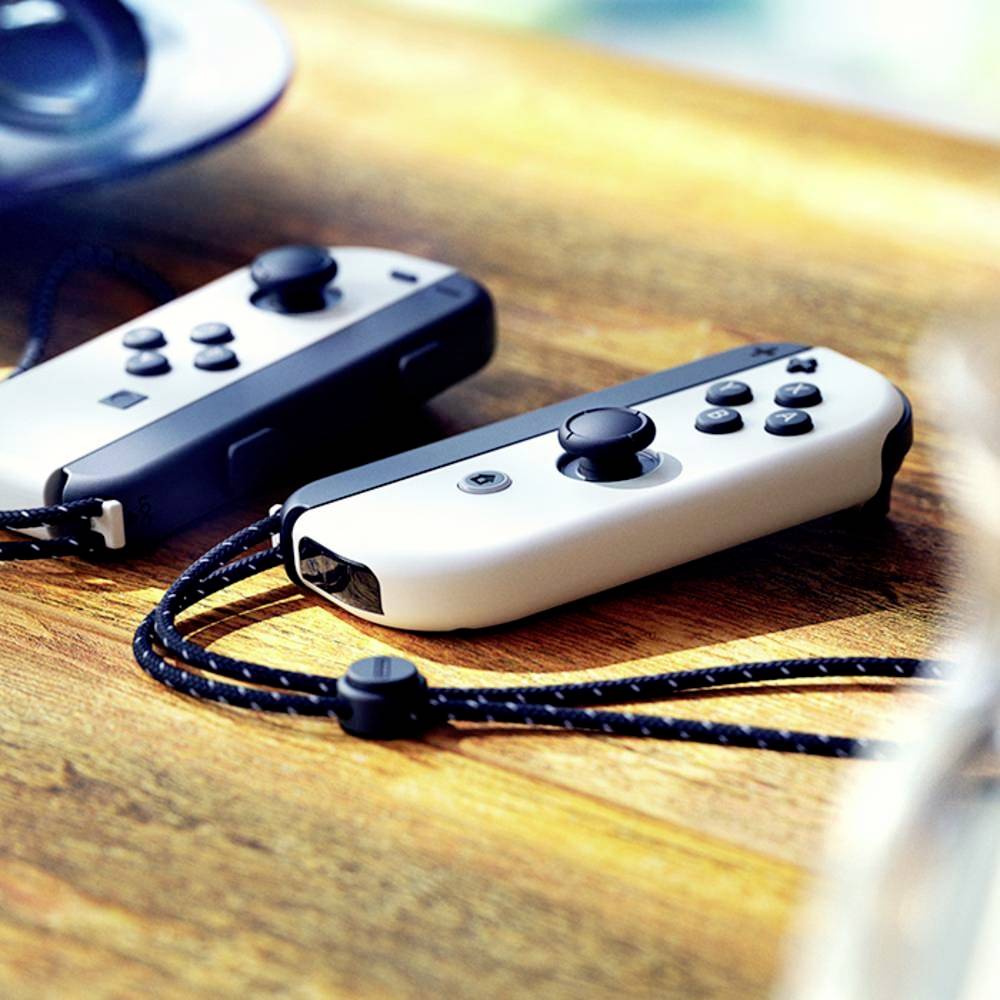 Zwei graue Spielcontroller liegen nebeneinander auf einem Holztisch, jeder mit einem Handgelenkband versehen.