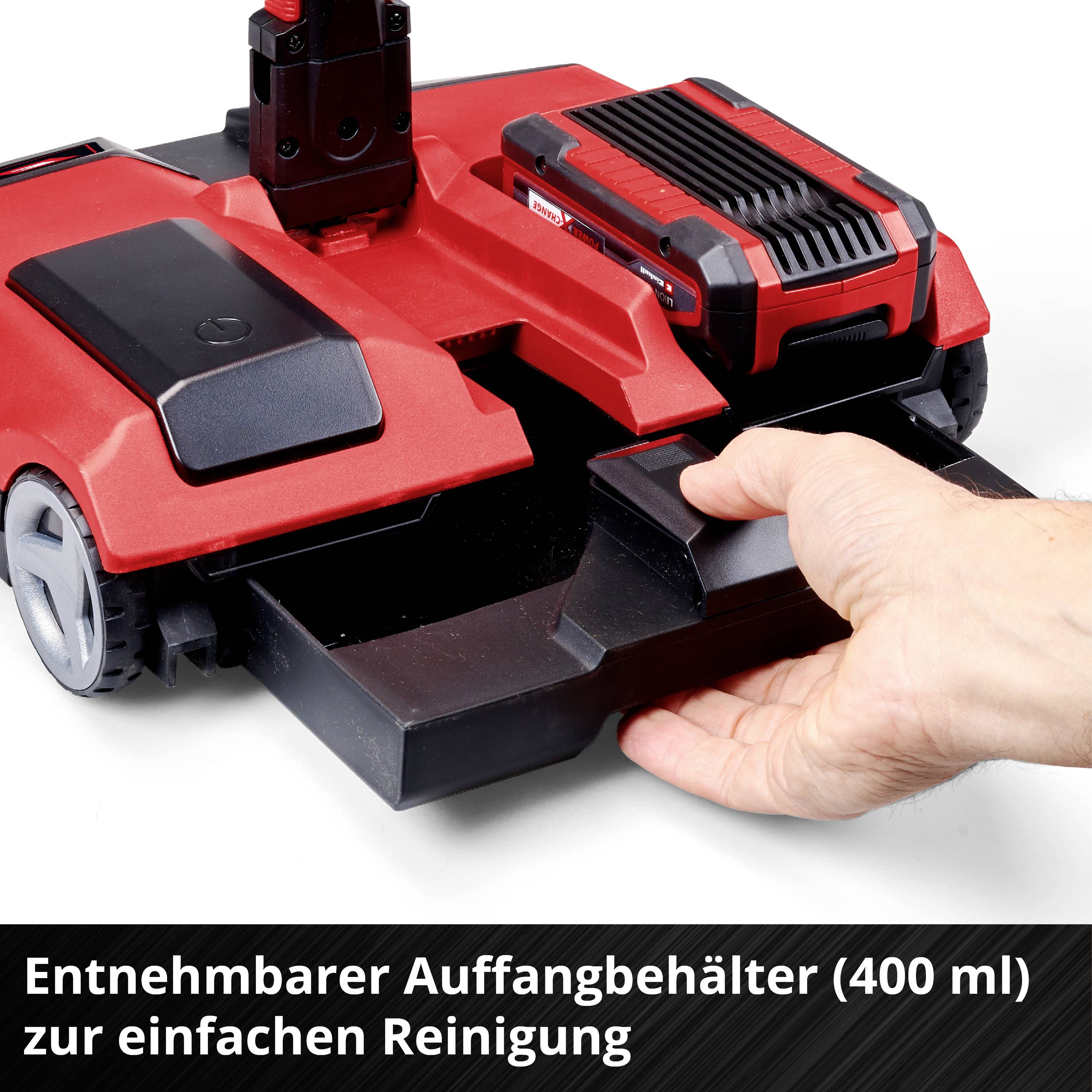 Rote Kehrmaschine mit entnehmbarem Auffangbehälter (400 ml) zur einfachen Reinigung. Eine Hand zeigt auf den geöffneten Behälter.