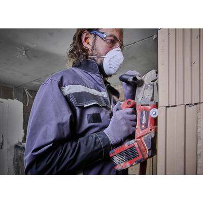 Person arbeitet mit Elektrowerkzeug an einer Wand. Schutzbrille, Maske und Handschuhe getragen. Renovierung oder Bauarbeiten.