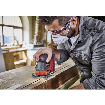 Ein Handwerker schleift in einer Werkstatt Holz mit einer elektrischen Schleifmaschine. Er trägt Schutzbrille und Maske.