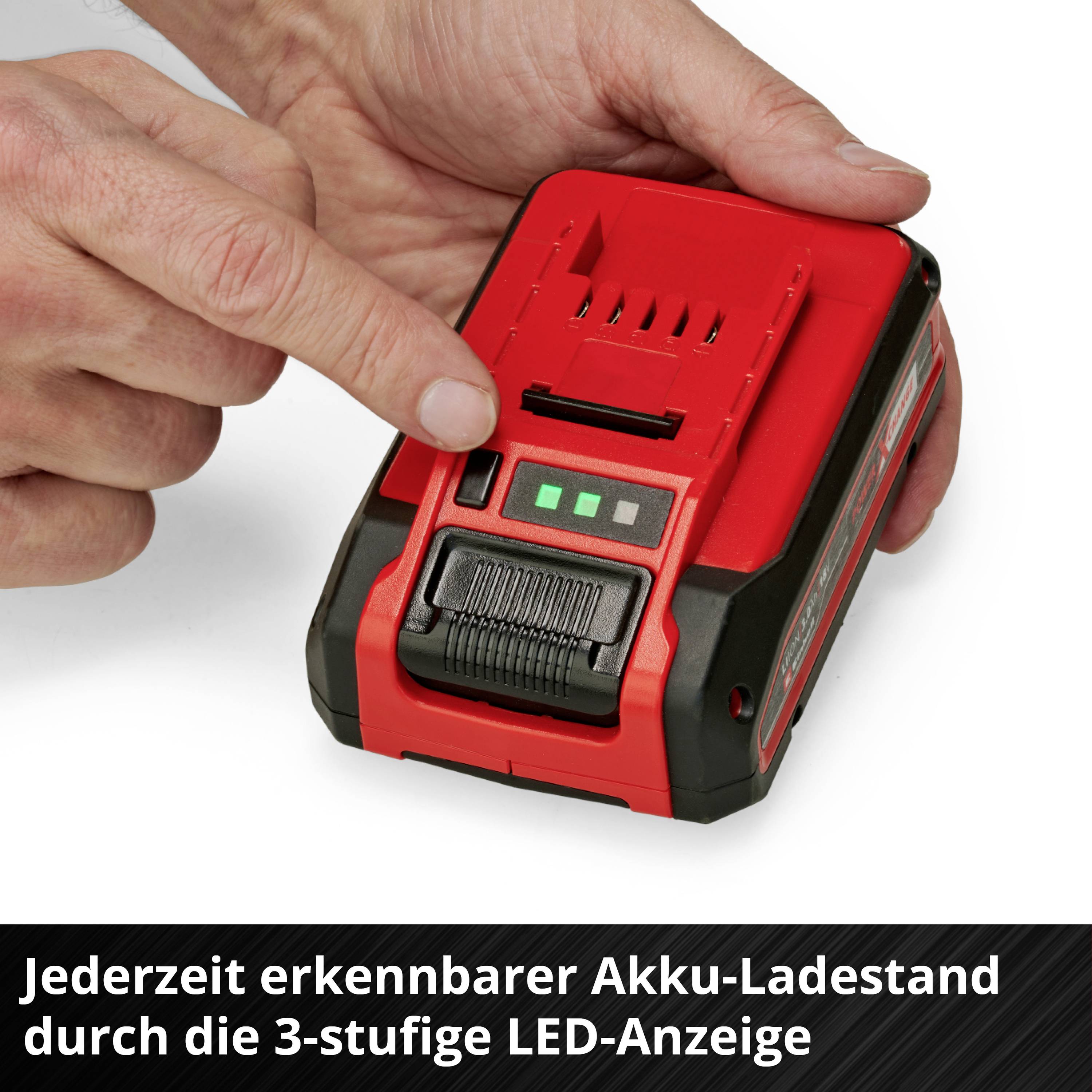 Eine Hand zeigt auf eine rote, tragbare Batterie mit drei grünen LED-Lichtern, die den Ladezustand anzeigen.