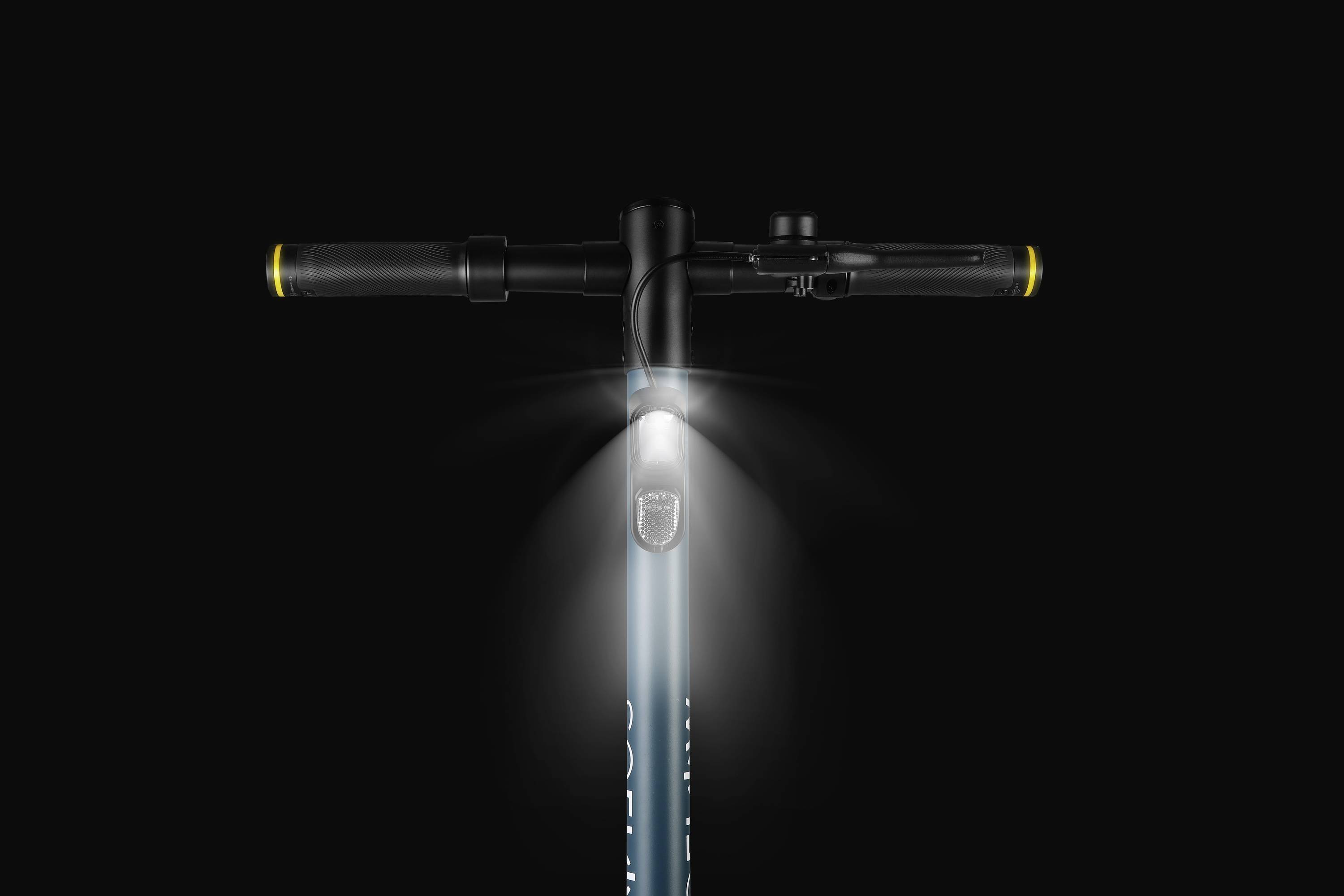 Nahaufnahme eines E-Scooter-Lenkers mit eingeschaltetem Frontlicht, dunkler Hintergrund.