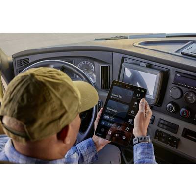 Ein Fahrer in einem LKW-Hybridecockpit hält ein Tablet mit Navigations-App. Das Display zeigt Optionen wie 'Karte anzeigen' und 'Wohin?'.