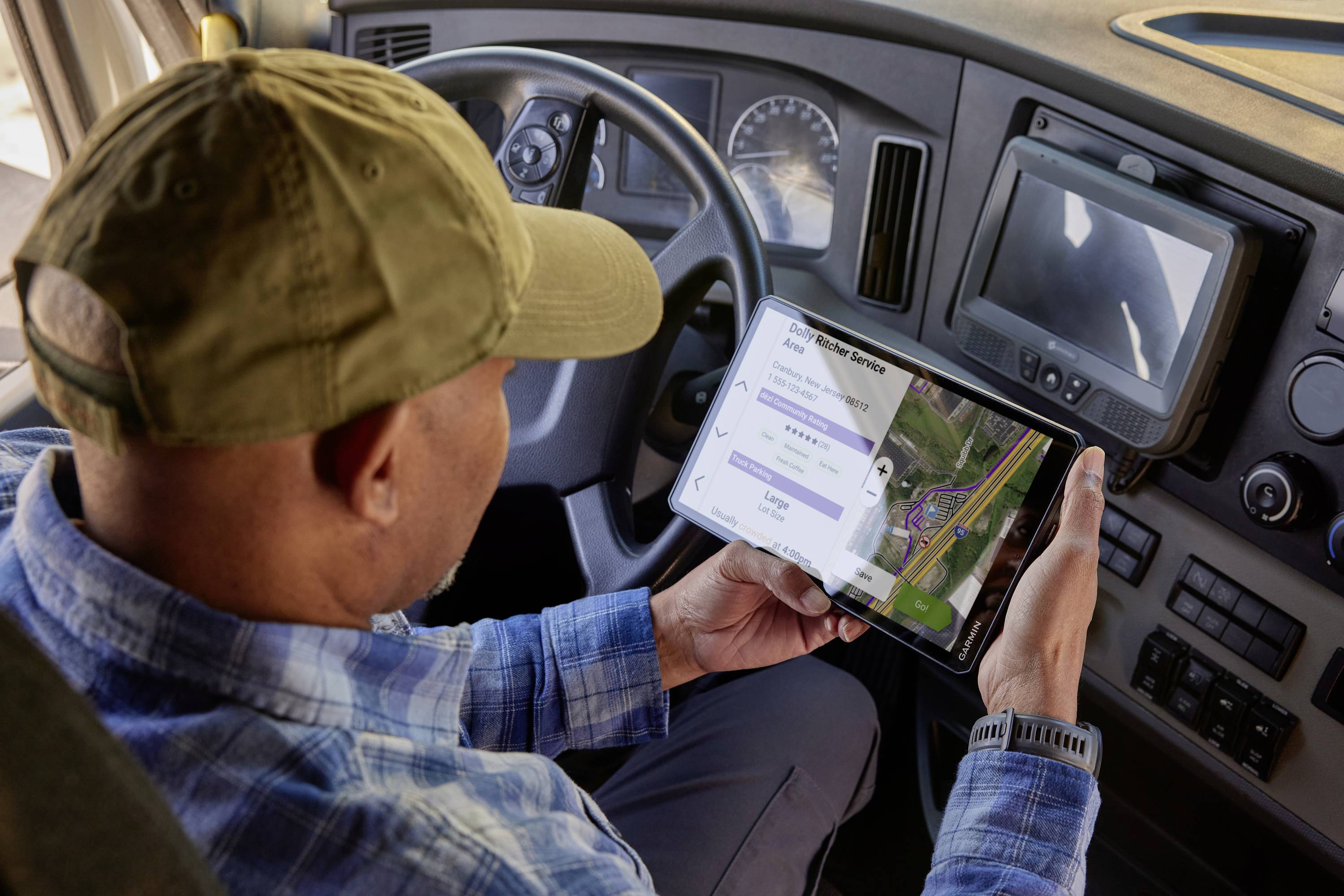 Ein Mann im Fahrerhaus eines Lkw schaut auf ein Tablet mit einer Navigationskarte und Routeninformationen.