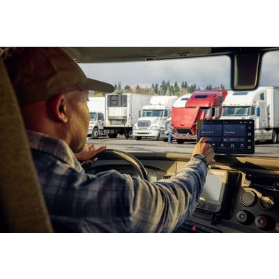Ein Lkw-Fahrer navigiert mit einem GPS-Gerät in einem Lkw-Parkplatz voller geparkter Lastwagen im Hintergrund.