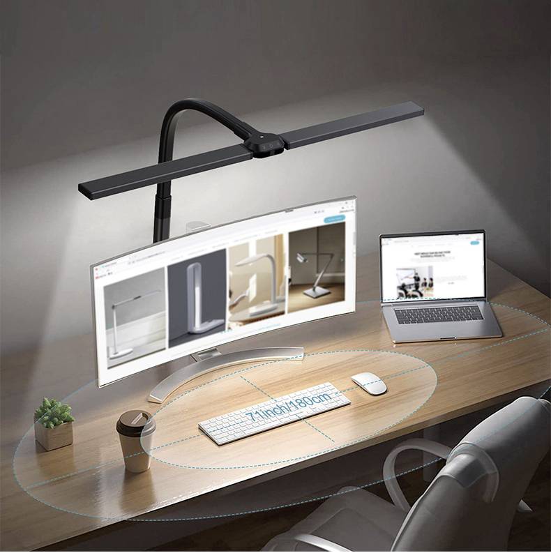 Ein Schreibtisch mit gebogener Lampe, zwei Monitoren, einer Tastatur und Maus. Eine Pflanze und eine Tasse stehen links.