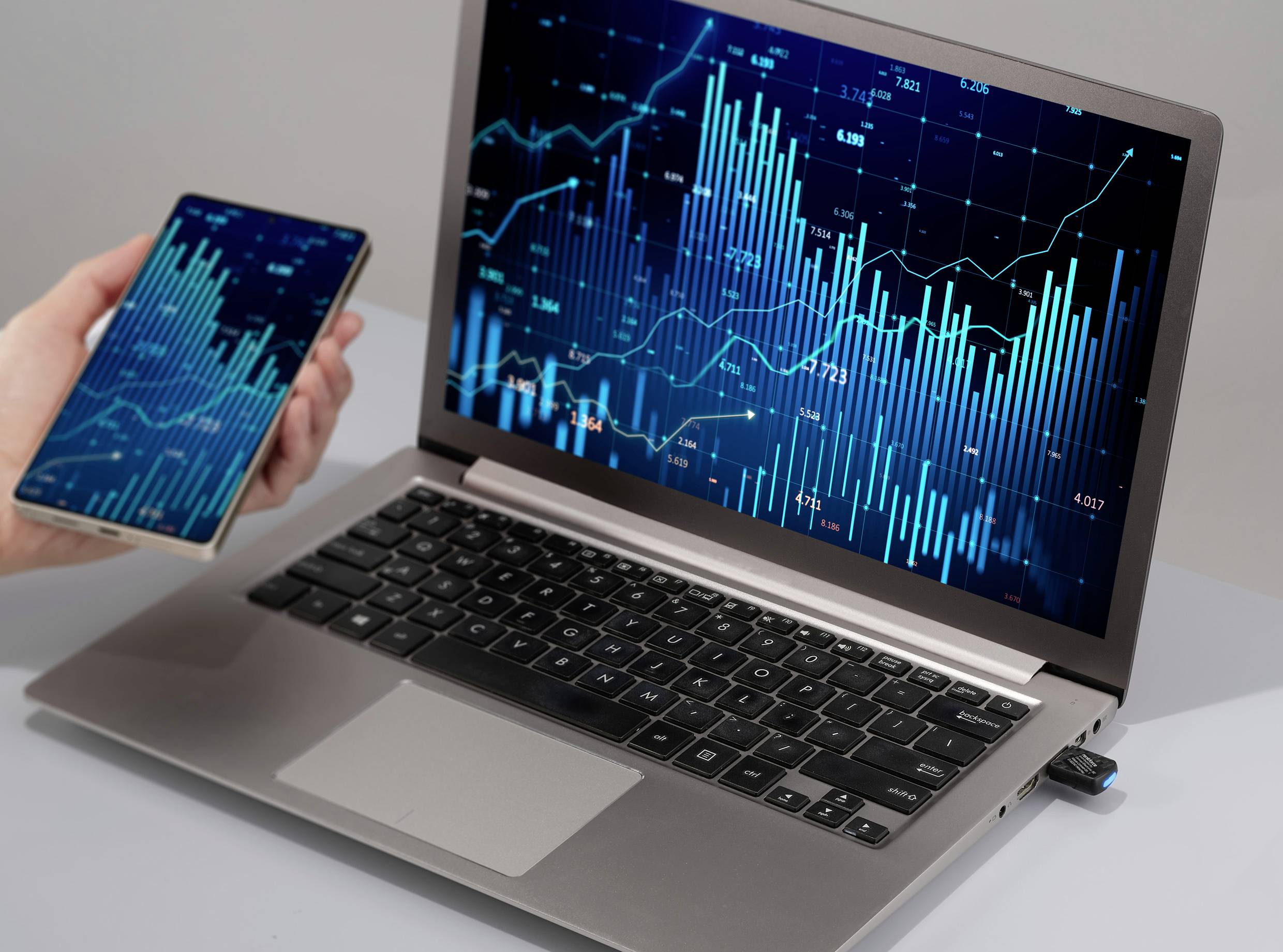 Ein Laptop und ein Smartphone zeigen komplexe Finanzdiagramme mit Balken und Linien, die Trends und Daten in Echtzeit darstellen.