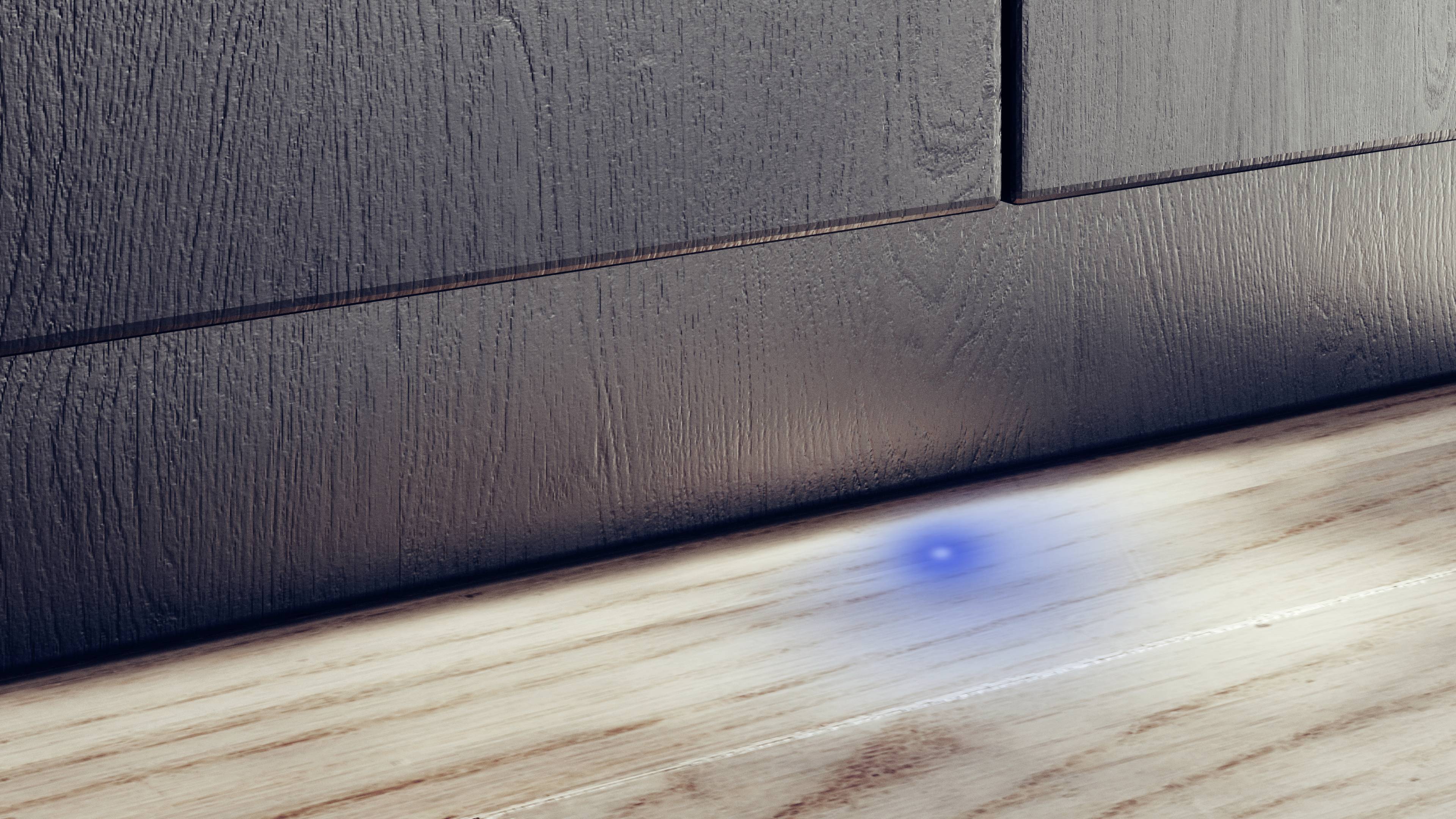 Eine minimalistische Küchensockelleiste mit Holzoptik und einer einzelnen blauen LED-Leuchte, die den Boden dezent beleuchtet.