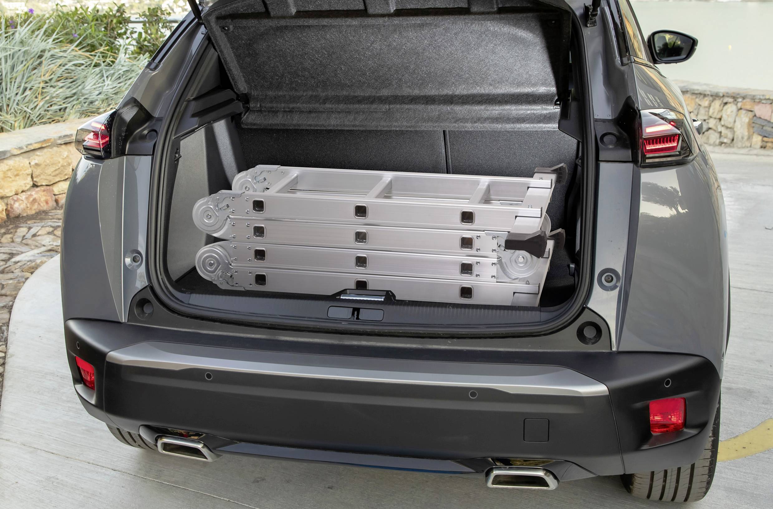 Ein graues Auto mit geöffneter Heckklappe. Im Kofferraum liegt eine zusammengefaltete Leiter.