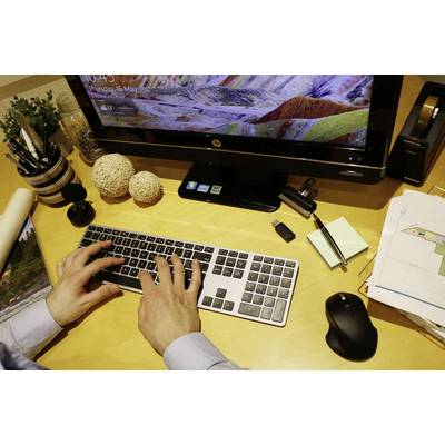 Person tippt auf einer Tastatur an einem Schreibtisch. Auf dem Bildschirm ist ein buntes Landschaftsbild zu sehen. Büroartikel liegen verstreut.