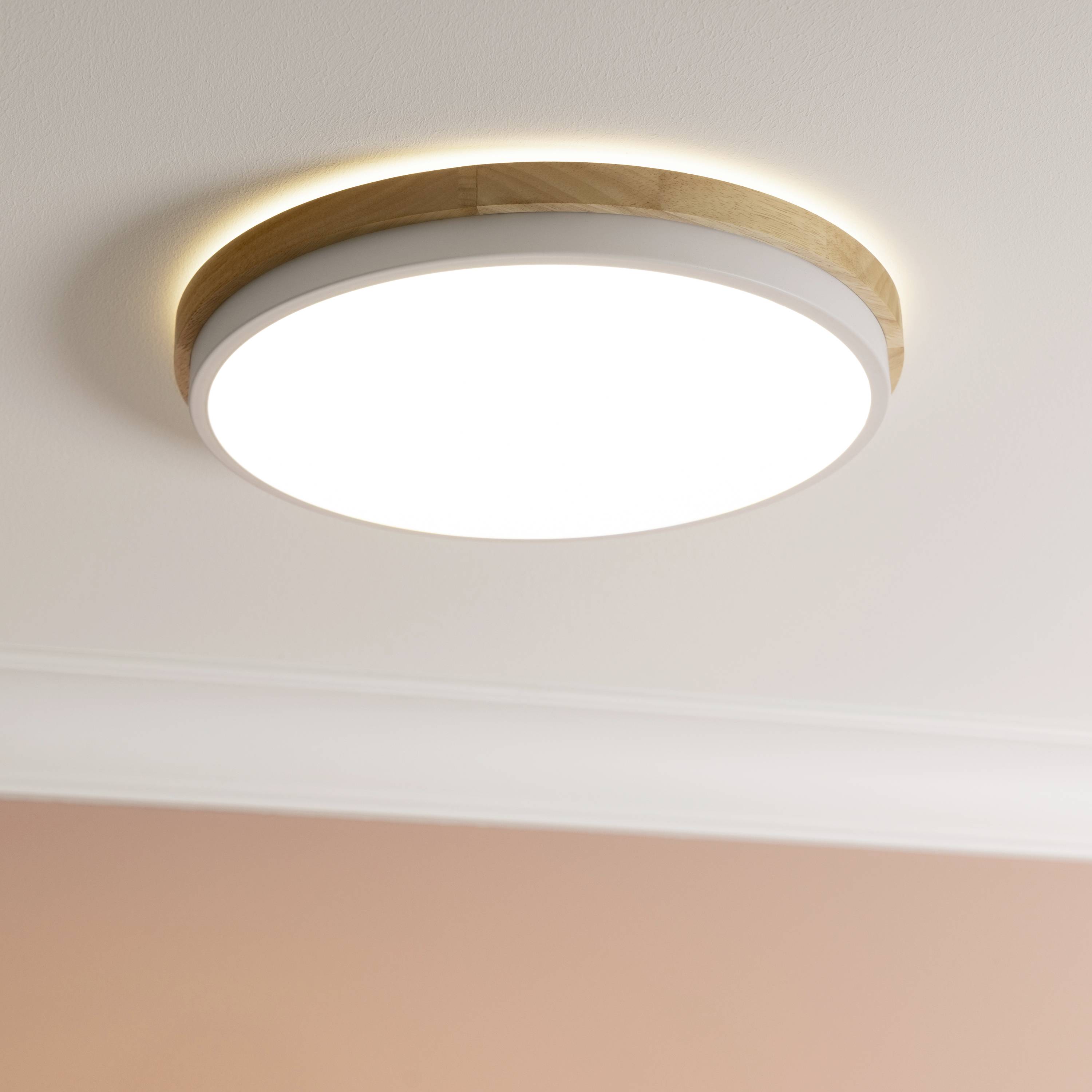Eine runde LED-Deckenleuchte, die warmweißes Licht in einem Raum mit rosa Wänden abstrahlt.