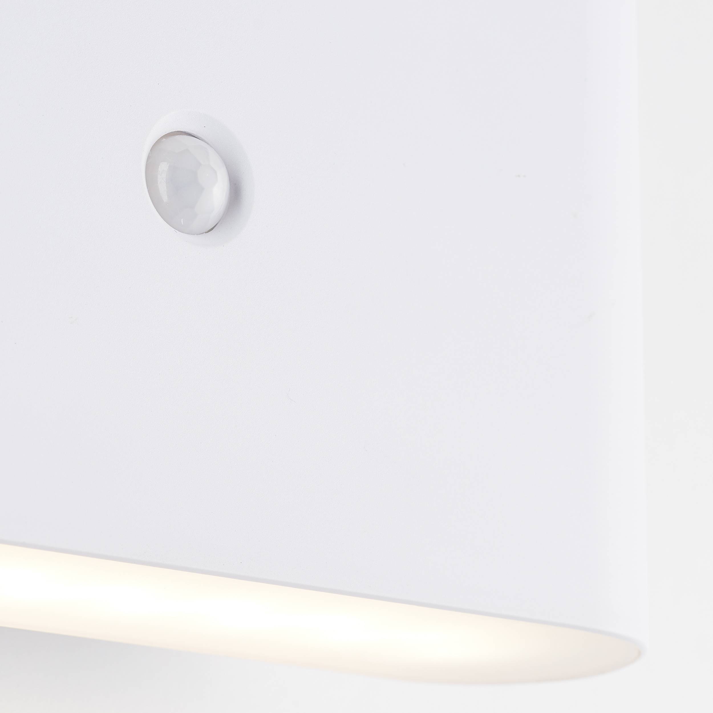 Eine minimalistische weiße Wandleuchte mit Bewegungsmelder oben und diffusem Licht unten, die eine moderne Atmosphäre schafft.