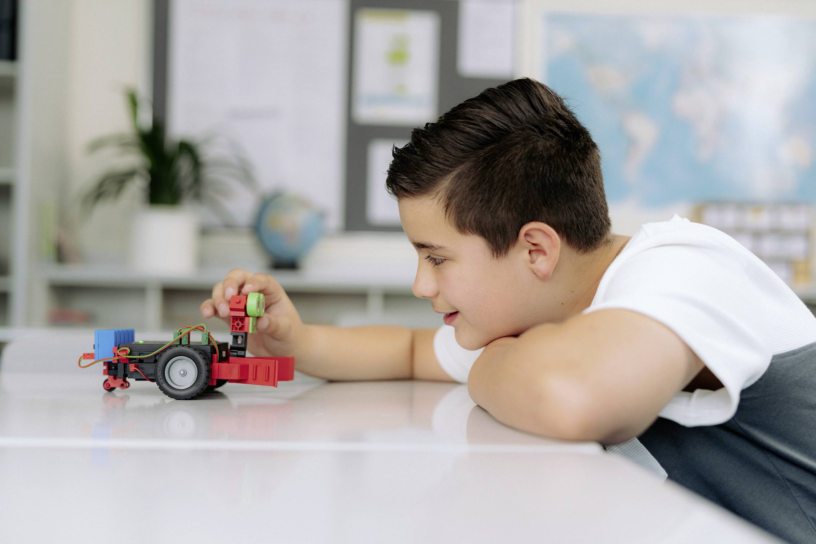 Ein Junge spielt und konzentriert sich auf ein kleines Roboterfahrzeug auf einem Tisch im Klassenzimmer.