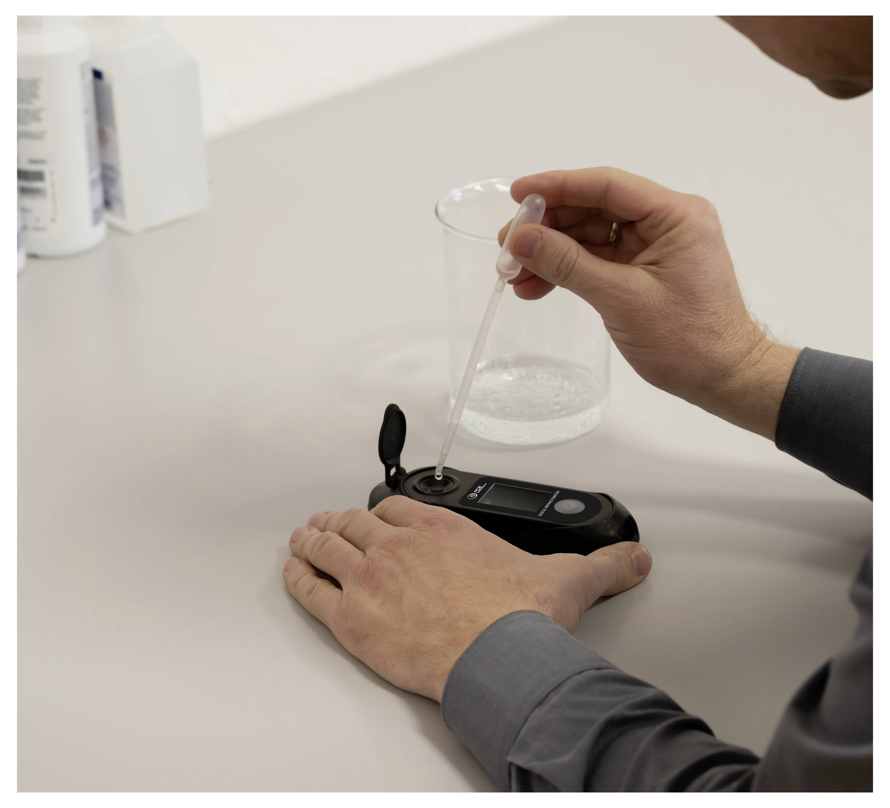 Person mit einer Pipette, die Flüssigkeit in ein tragbares digitales Messgerät auf einem Tisch während eines Labortests überträgt.