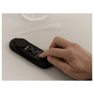 Eine Hand legt ein schwarzes Blutzuckermessgerät auf einen Tisch; ein Teststreifen liegt darüber und deutet auf einen Bluttest hin.