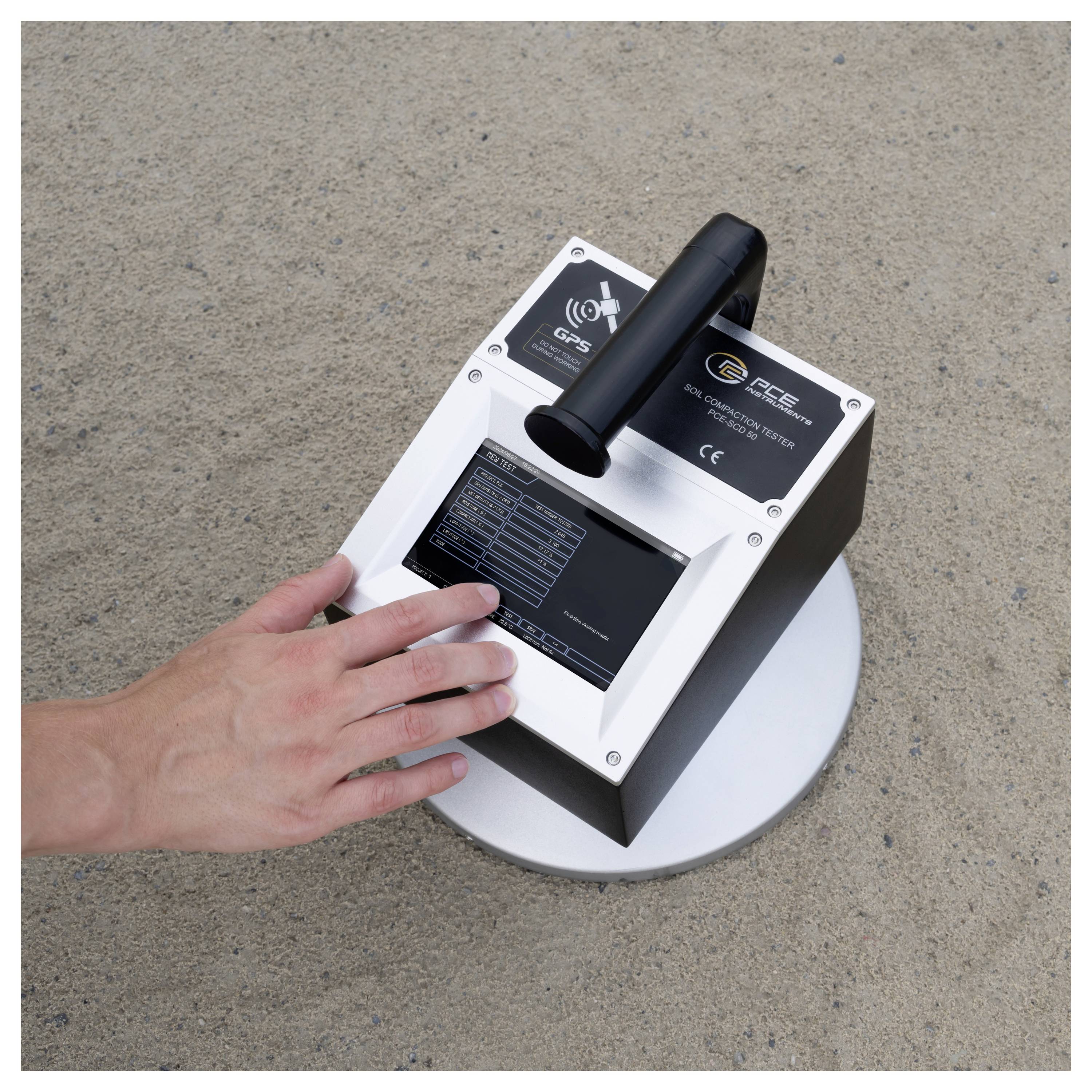Hand mit einem tragbaren GPR-Bodenscanning-Gerät auf Asphalt, mit sichtbarem Griff und Display-Bildschirm.