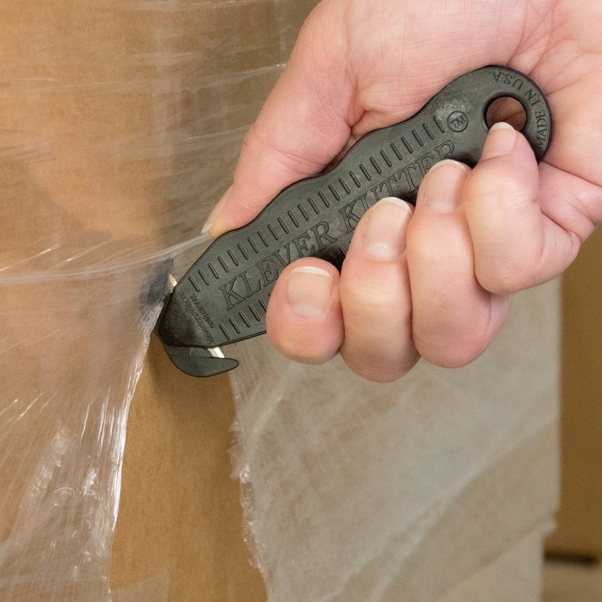 Hand hält Sicherheitsmesser, schneidet Karton. Schneideblatt verbirgt, reduziert Verletzungsrisiko.