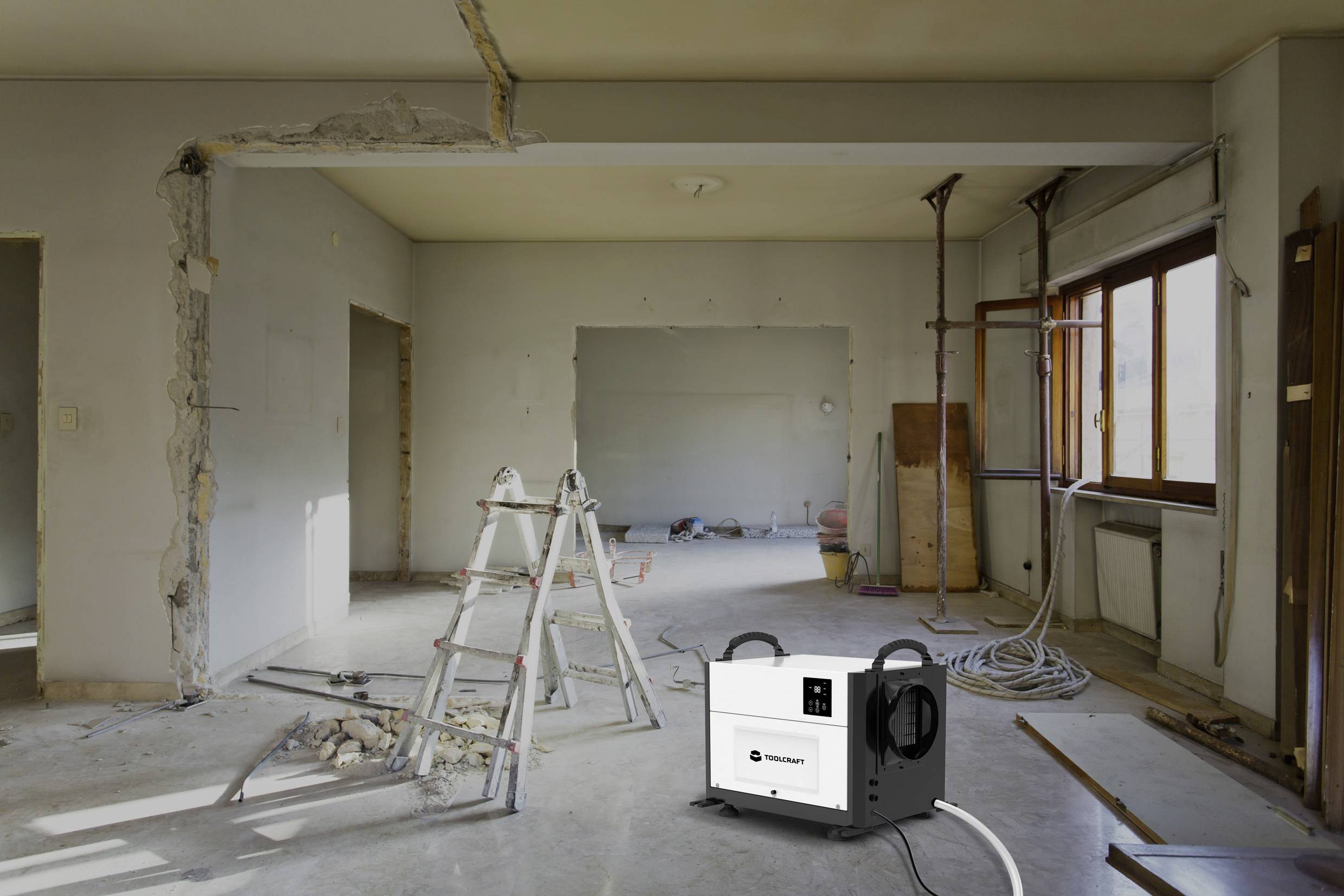 Ein halb renovierter Raum mit offenen Wänden und einer Leiter in der Mitte. Ein Baustellenentfeuchter steht im Vordergrund.