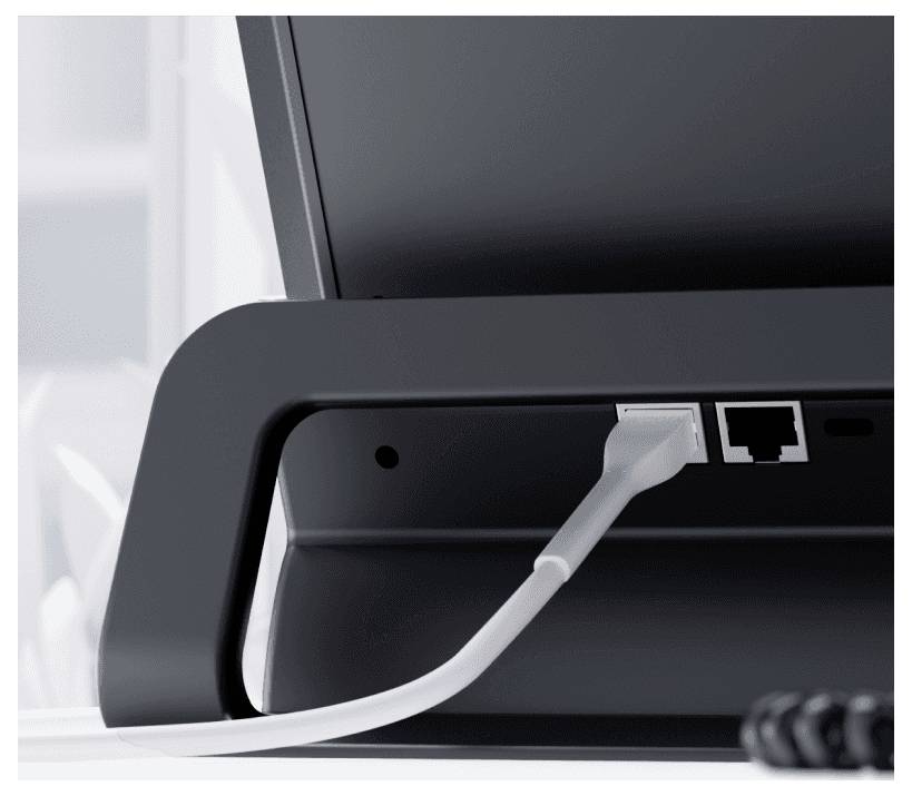 Ein weißes Kabel ist in den LAN-Port eines schwarzen Monitors eingesteckt, der auf einem Schreibtisch steht.