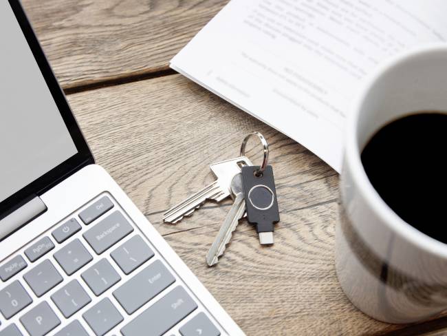 Laptop, Schlüsselbund mit USB-Stick, Tasse Kaffee und Papiere auf einem Holztisch. Schreibtischarbeitsbereich im Büro.