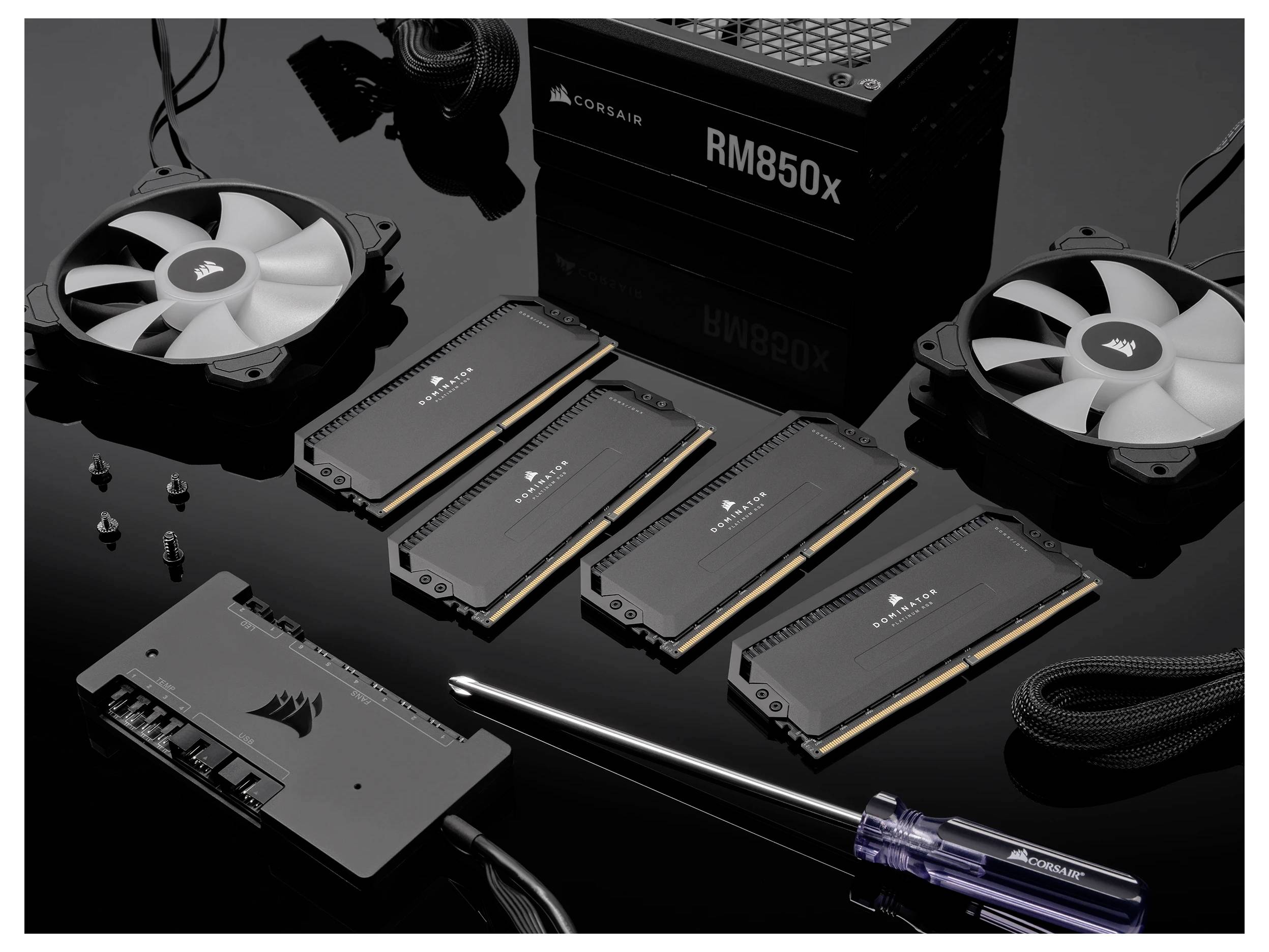 'Ein Computerhardware-Setup mit vier RAM-Riegeln, zwei Lüftern, einem Netzteilmodul und einem Schraubenzieher auf schwarzem Hintergrund.'